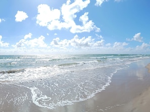 Une plage avec des vagues, un ciel dégagé et des nuages.