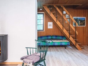 A room with a wooden staircase, a green chair, a sofa with a plaid cover, and a fireplace.