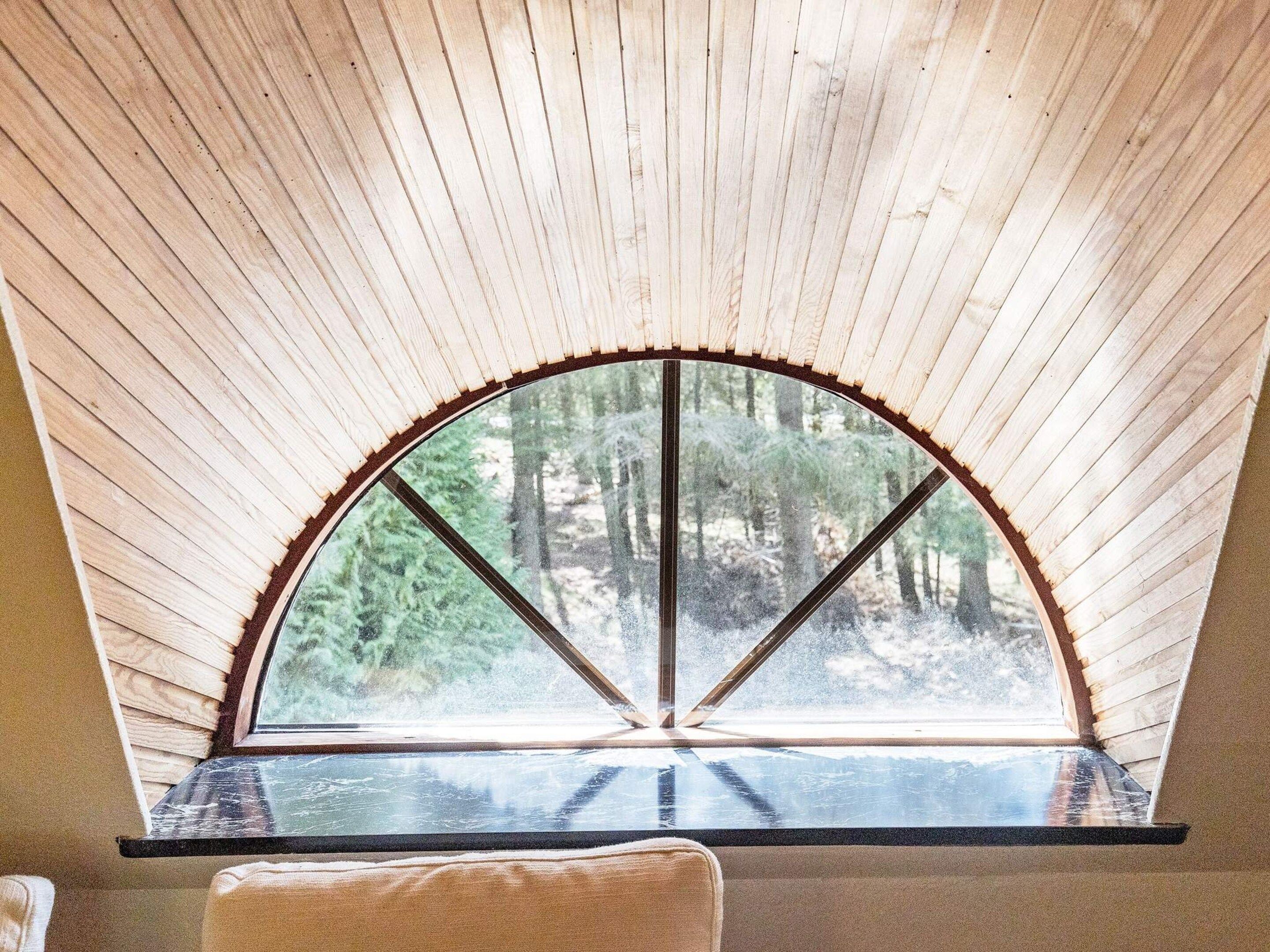 A room with a large arched window overlooking a forest.