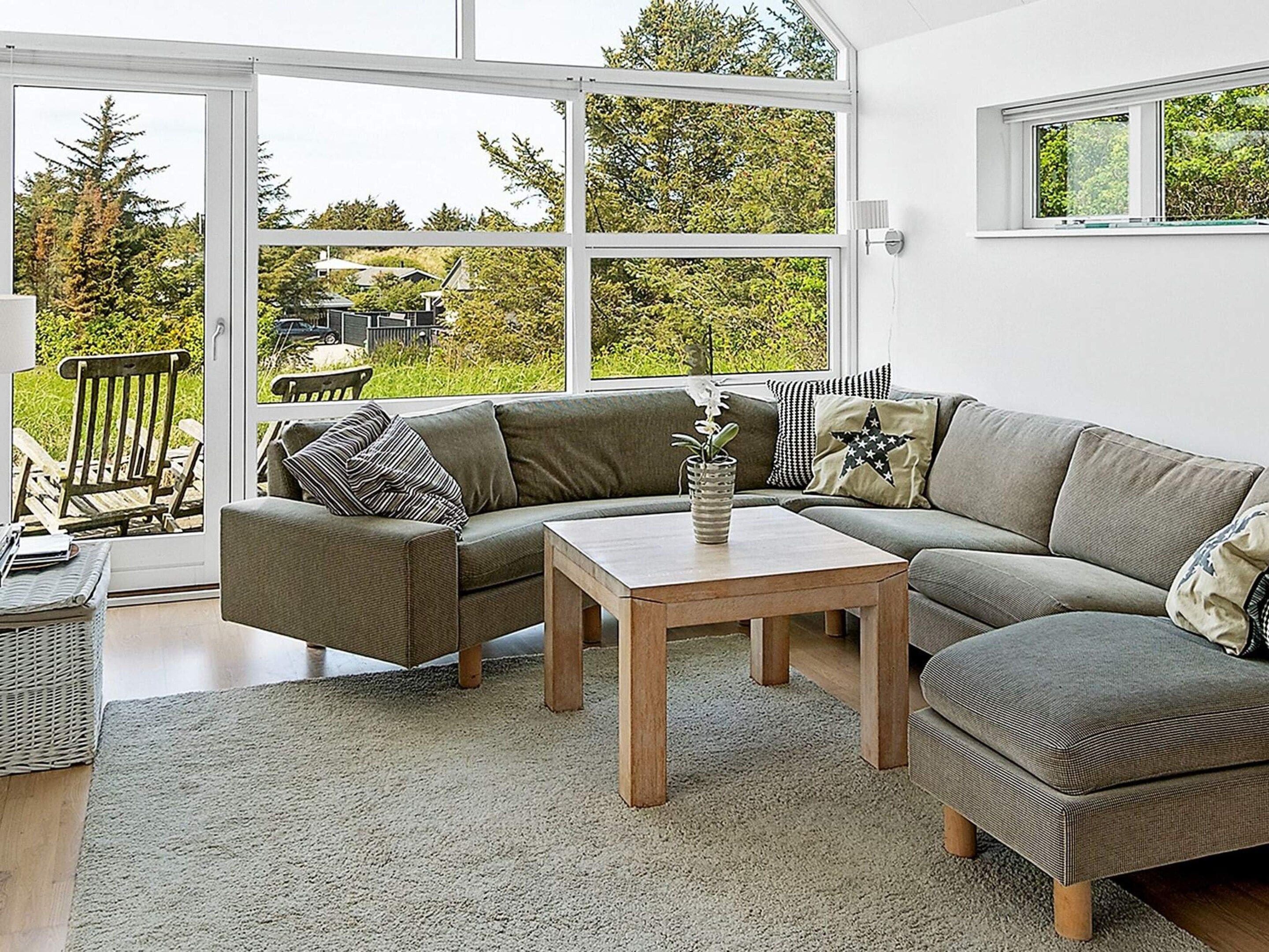 A modern living room with a sectional sofa, a coffee table, and a view of a garden through large windows.