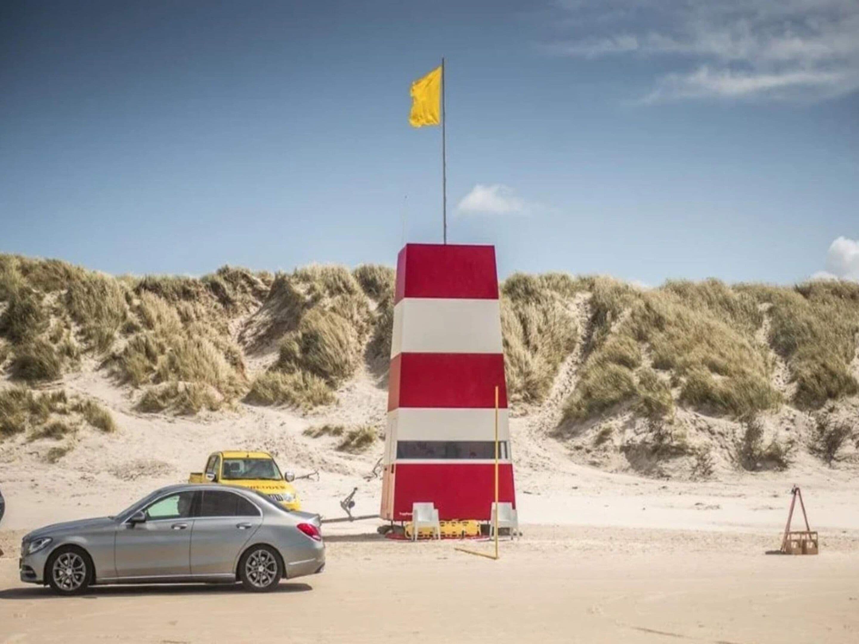 Ein Strand mit einem Rettungsturm, einem Auto und einer gelben Flagge.