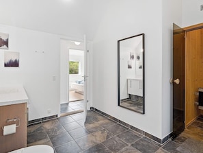 A hallway with a bed, a mirror, and a door leading to a bathroom. - Holiday Home in Blokhus (Blokhus)