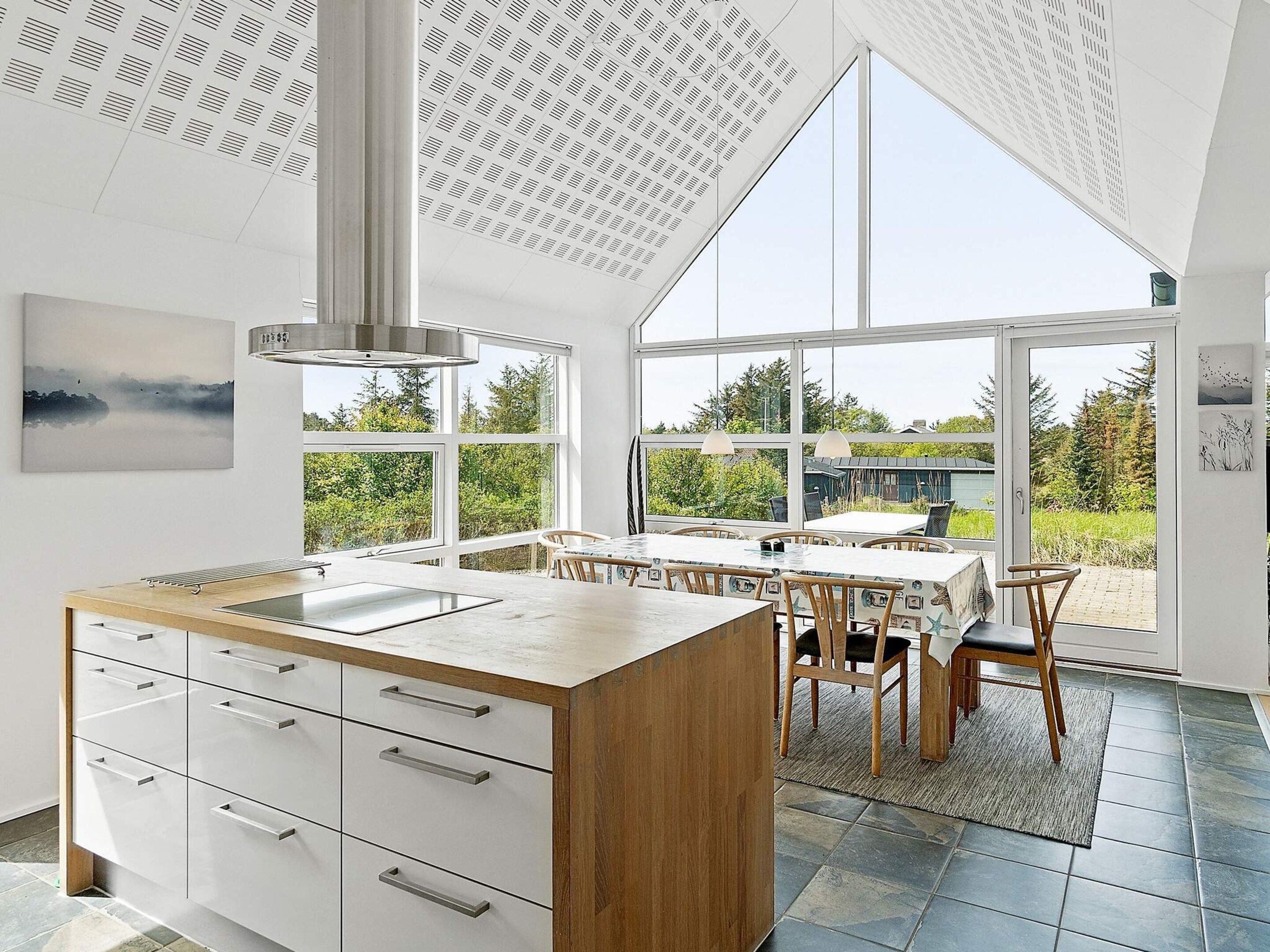 Eine moderne Küche mit einer großen Kochinsel, weißen Schränken und Blick durch große Fenster.