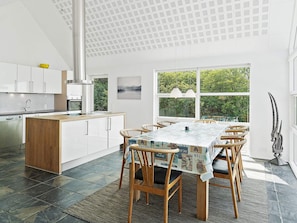 A modern kitchen with white cabinets, a wooden island, and a dining area with a table set for six. - Holiday Home in Blokhus (Blokhus)