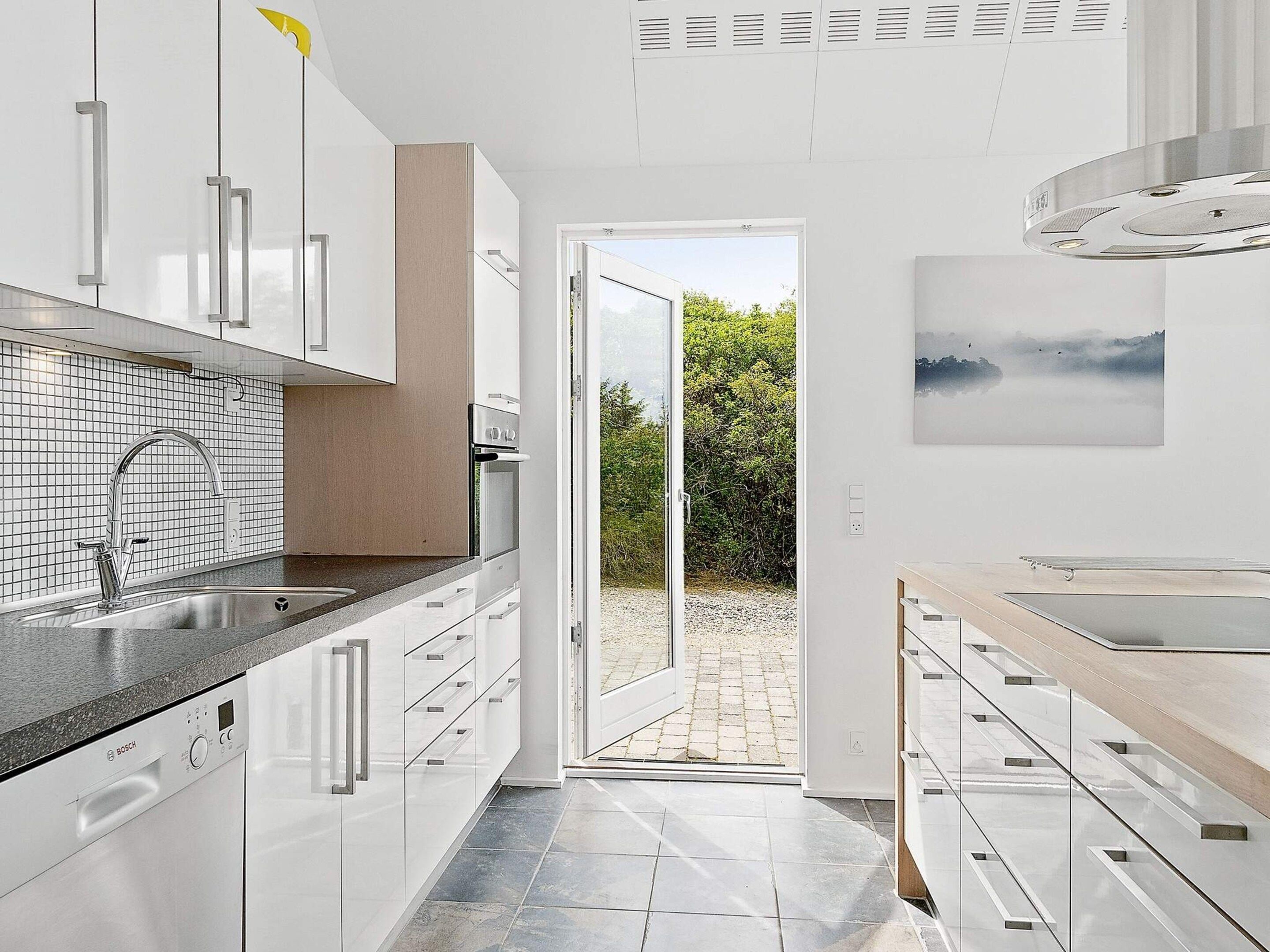 Une cuisine moderne avec des meubles blancs, un lave-vaisselle Bosch et une vue sur l’extérieur.