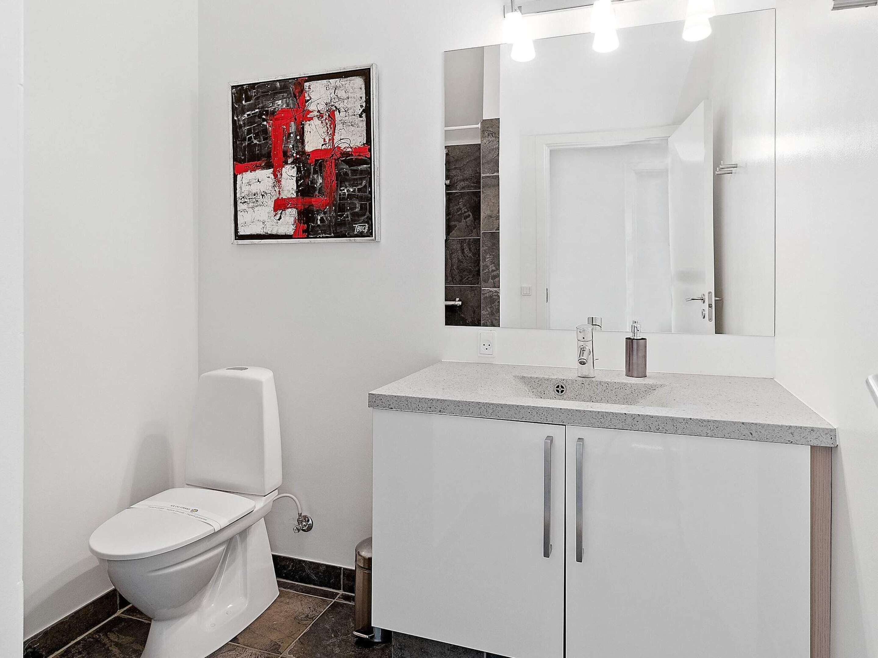 A modern bathroom with a white toilet, a granite countertop sink, and a large mirror above the sink.