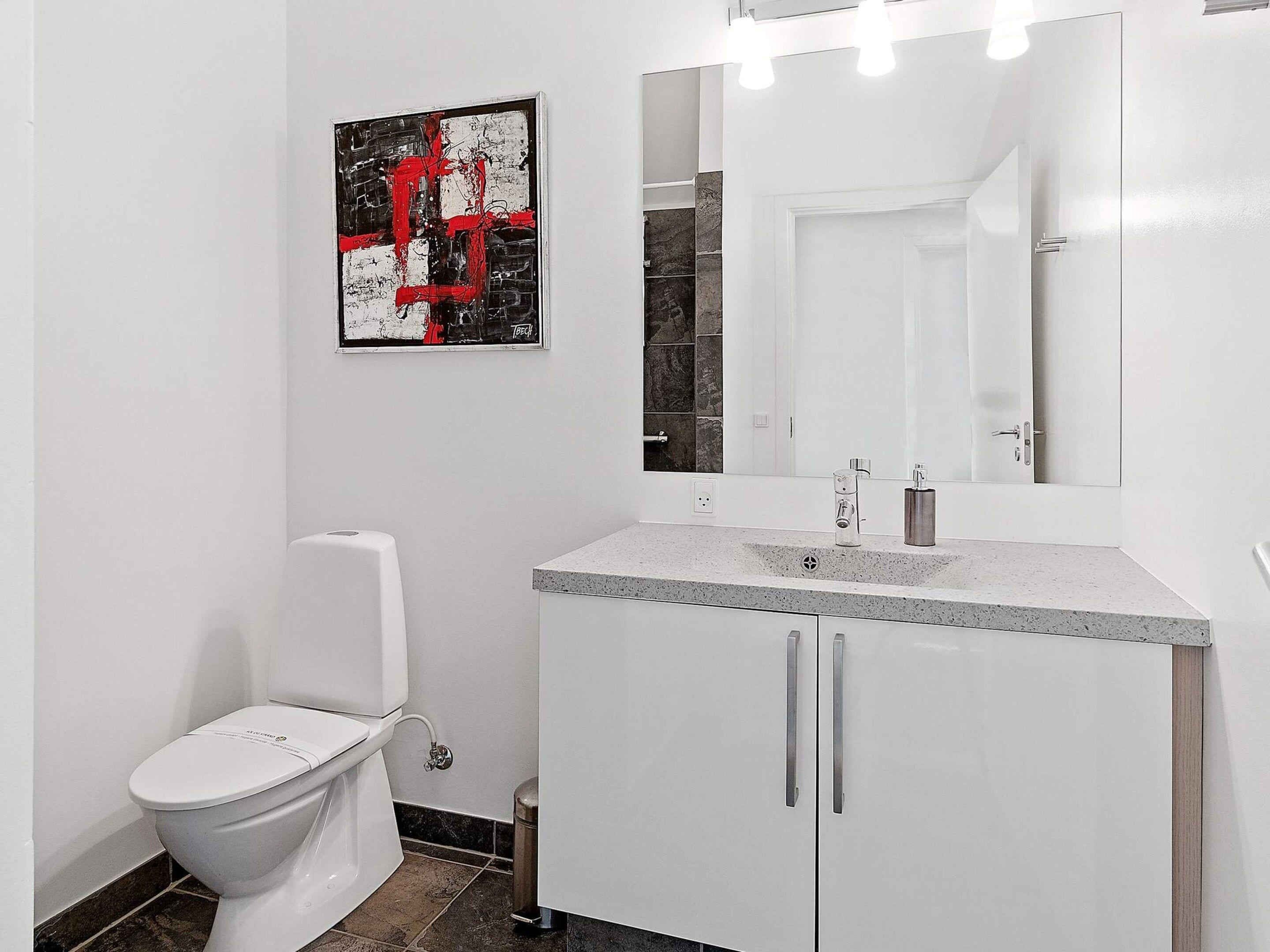 A modern bathroom with a white toilet, a granite countertop sink, and a large mirror.
