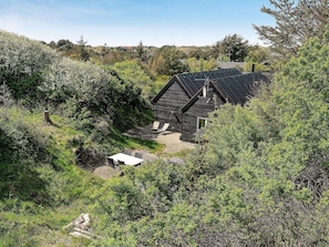 A wooden cabin with a sloped roof, surrounded by dense greenery and trees.