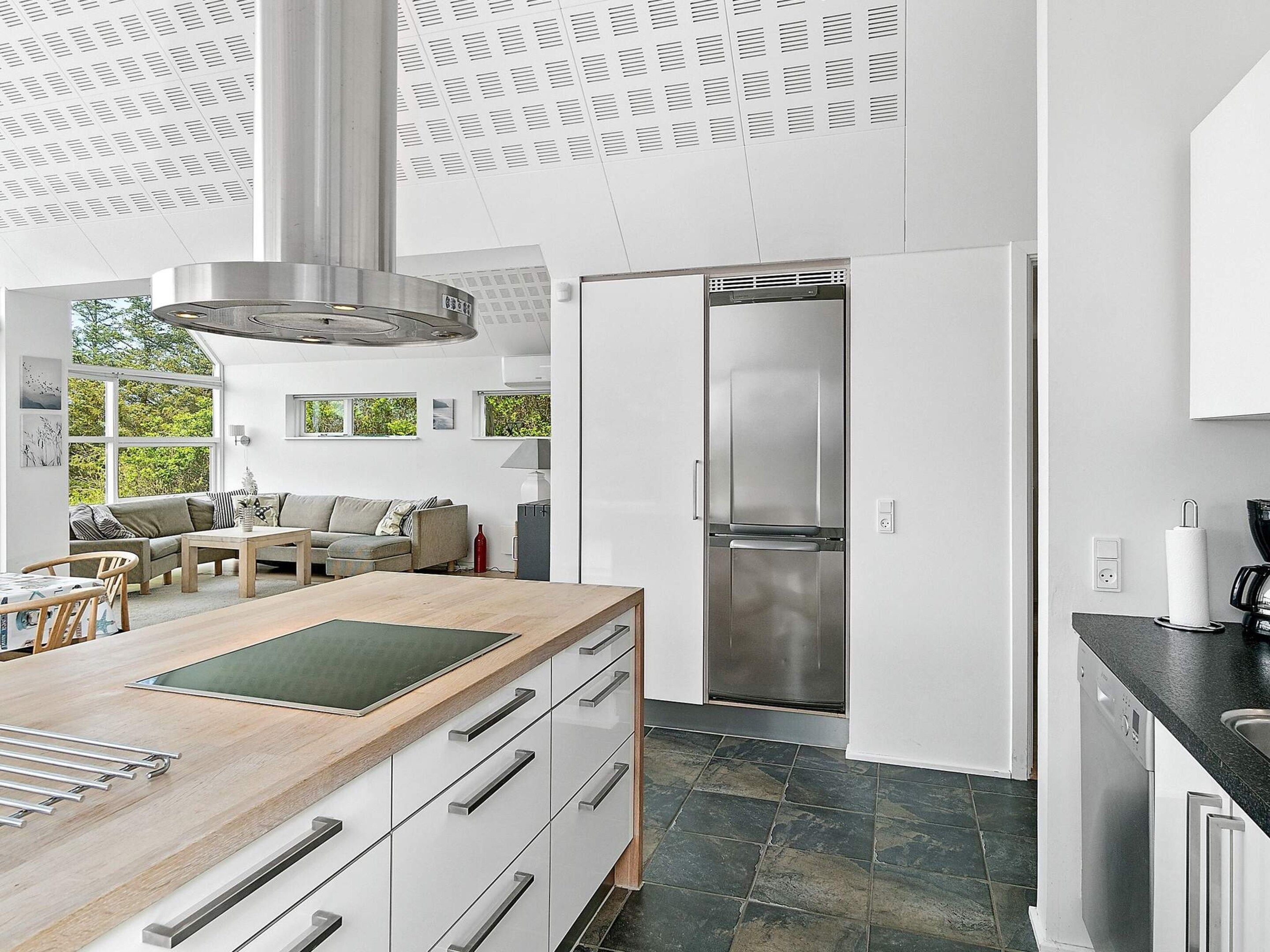 A modern kitchen with a large island, stainless steel appliances, and a view of greenery outside.