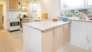 A modern kitchen with wooden cabinets, a central island, and a large window providing a view of the outside. - 7 Person Holiday Home in Frederikshavn (Frederikshavn)