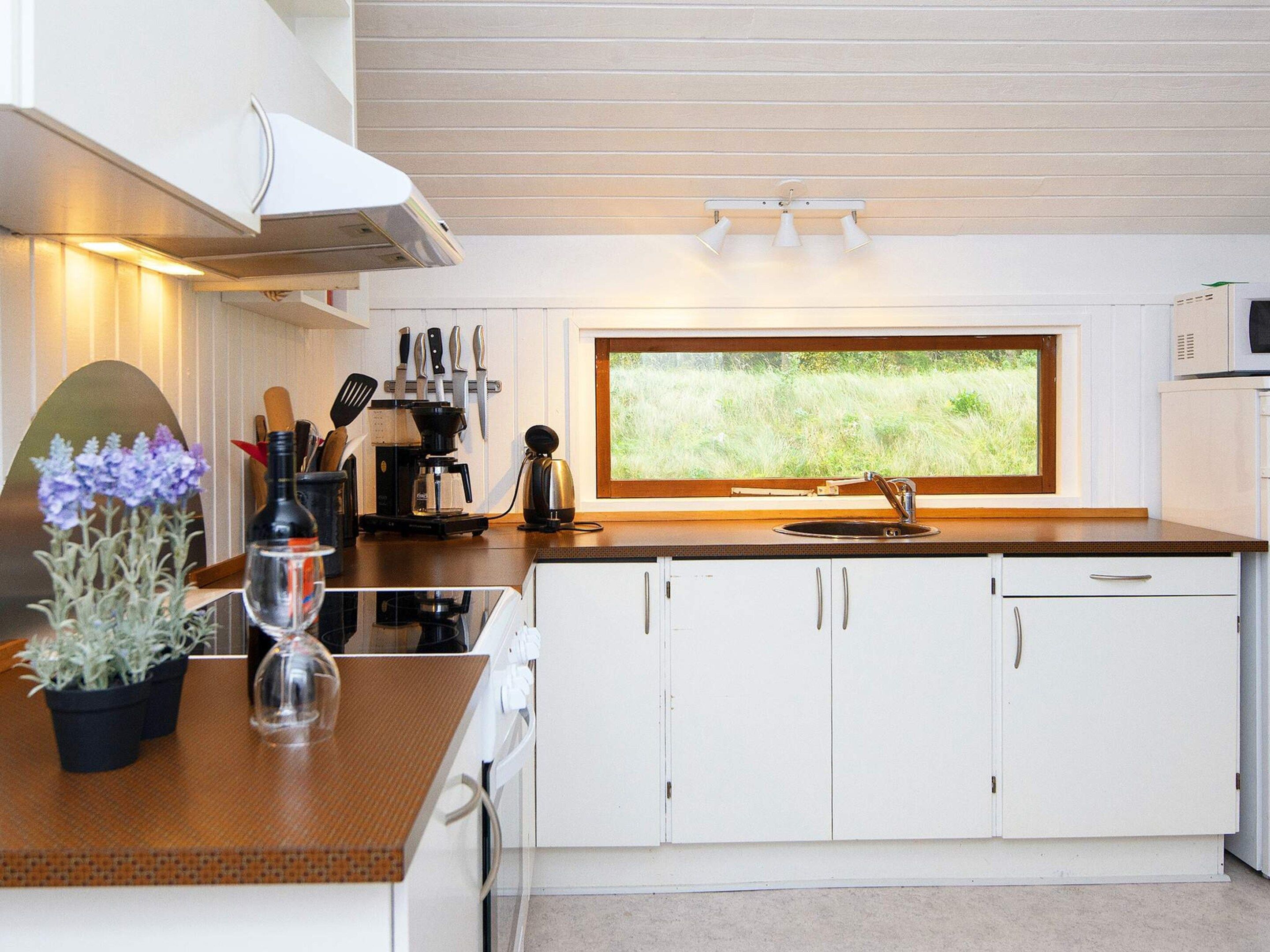 Een moderne keuken met witte kastjes, een groot raam en uitzicht op groen.
