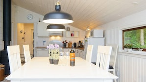 A modern kitchen with white cabinetry, a dining table with chairs, a large pendant light, and a view of greenery outside. - 6 Person Holiday Home in Farvang (Farvang)