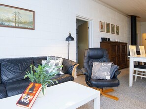 Un salon avec un canapé en cuir, une table basse blanche, un fauteuil en cuir noir et une table à manger avec des chaises. On trouve une plante sur la table basse et un tableau au mur.