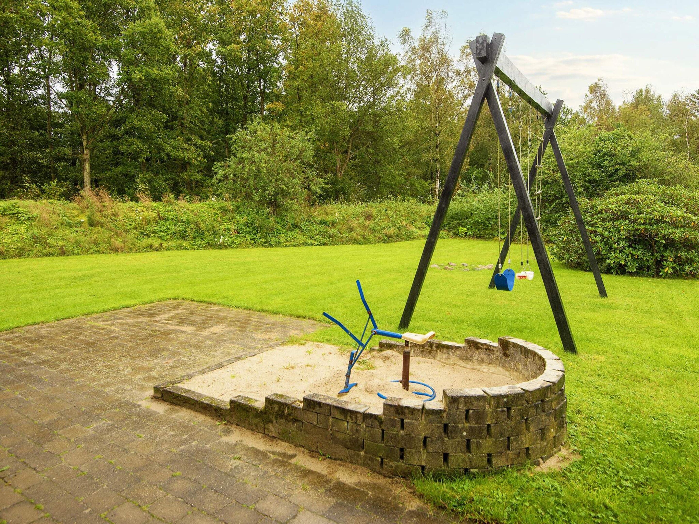 Eine Schaukel auf einer Wiese mit einem Backsteinbau in der Nähe.