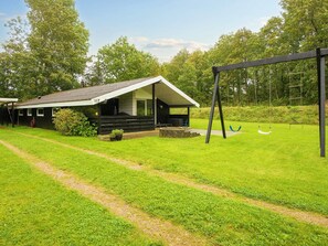 A cabin with a porch, a swing set, and a grassy yard. - 6 Person Holiday Home in Farvang (Farvang)
