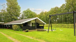 A cabin with a porch, a swing set, and a well-maintained lawn. - 6 Person Holiday Home in Farvang (Farvang)