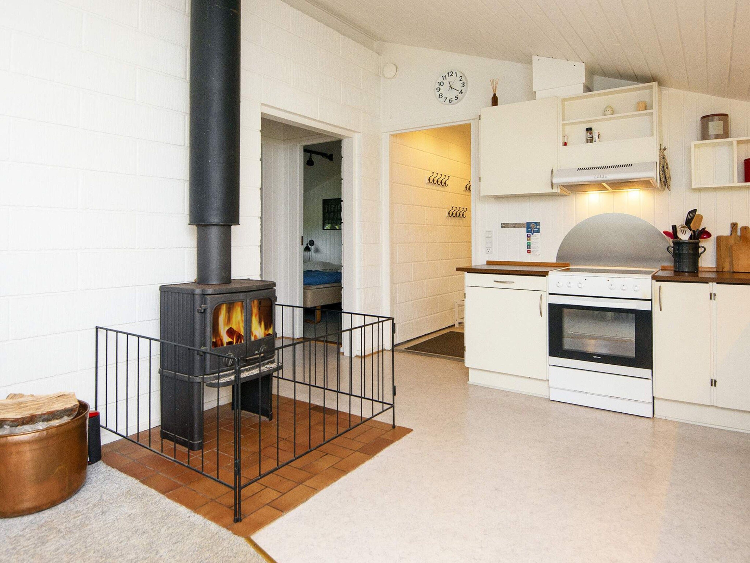 A modern kitchen with a wood-burning stove, white cabinetry, and a clock on the wall.