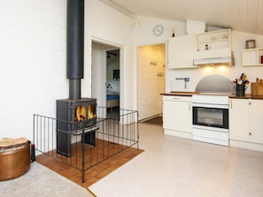 A modern kitchen with a wood-burning stove, white cabinetry, and a clock on the wall.