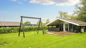 A grassy outdoor area with a swing set and a covered structure.