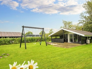 A grassy outdoor area with a swing set and a covered structure.