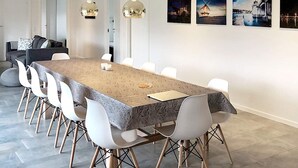 Ein moderner Essbereich mit einem langen Tisch, weißen Stühlen und Pendelleuchten.