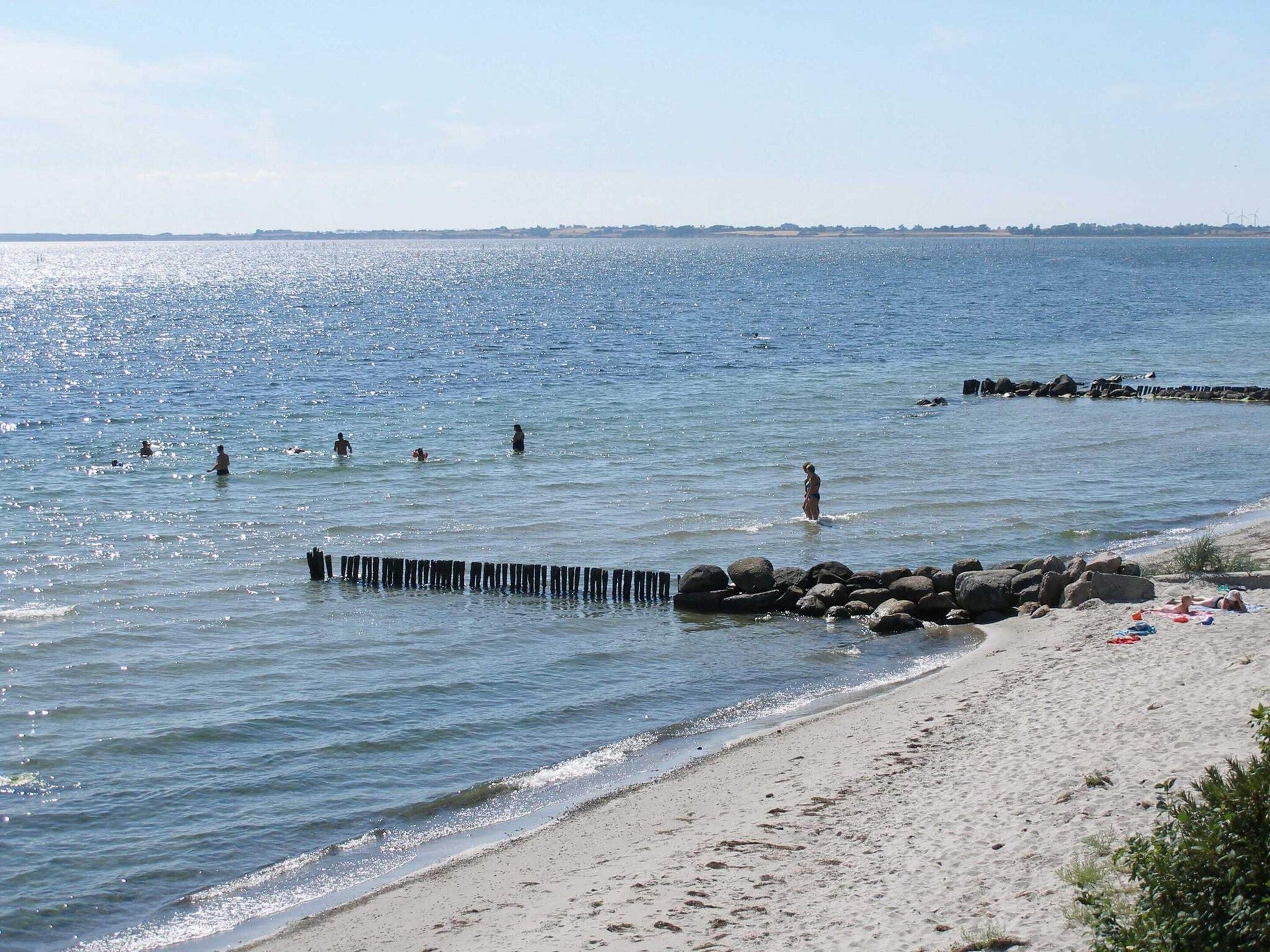Una spiaggia con acque limpide, persone che nuotano e un molo roccioso.