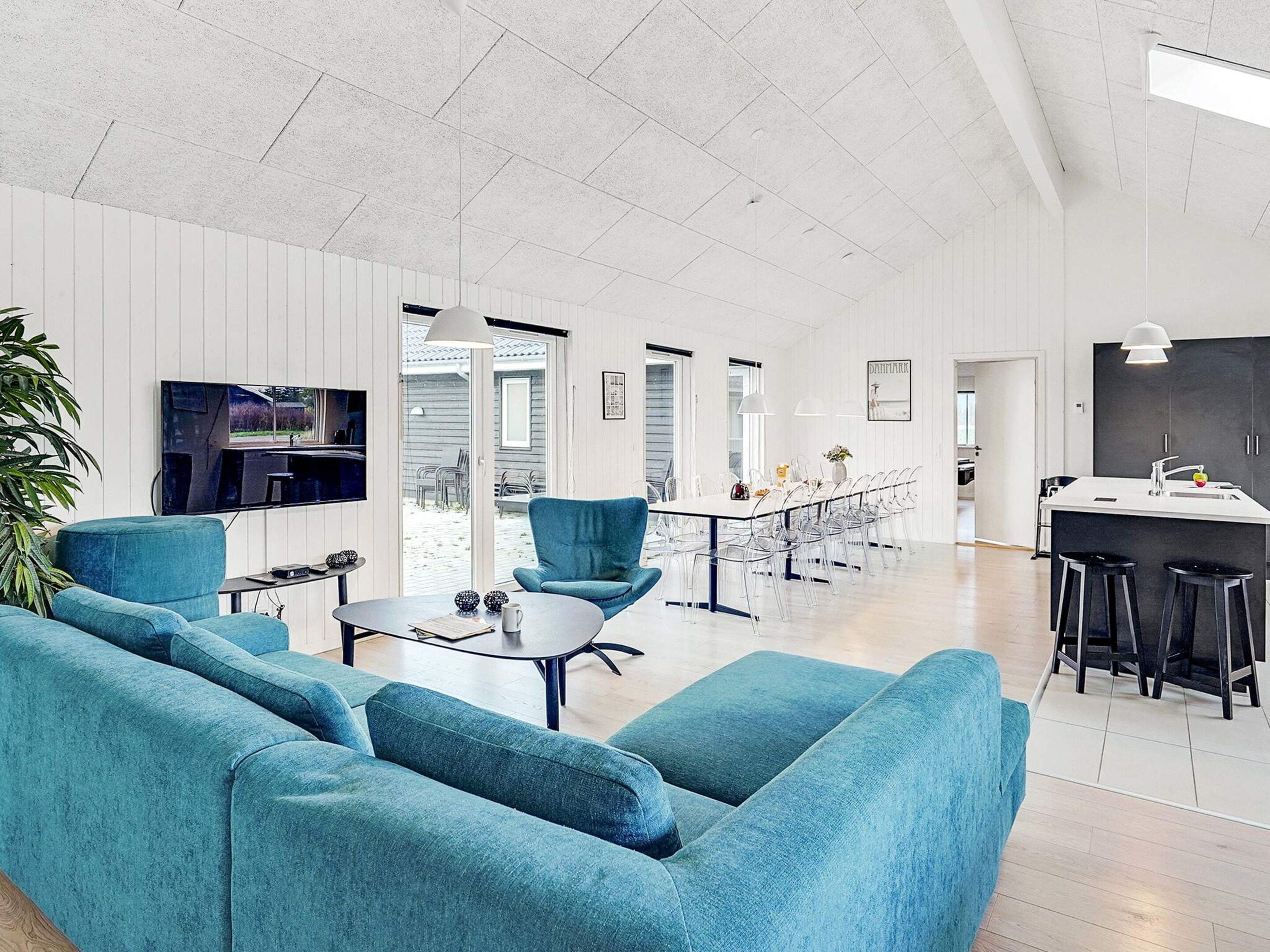 Amplia sala de estar con un amplio sofá, una mesa de comedor con sillas y una zona de cocina con barra.
