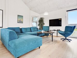 A modern living room with a sectional sofa, a round coffee table, a blue armchair, and a large window offering a view.