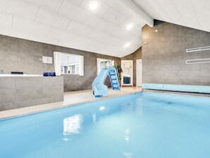 Una piscina interior con un tobogán azul, una recepción y una puerta que da a un vestuario.
