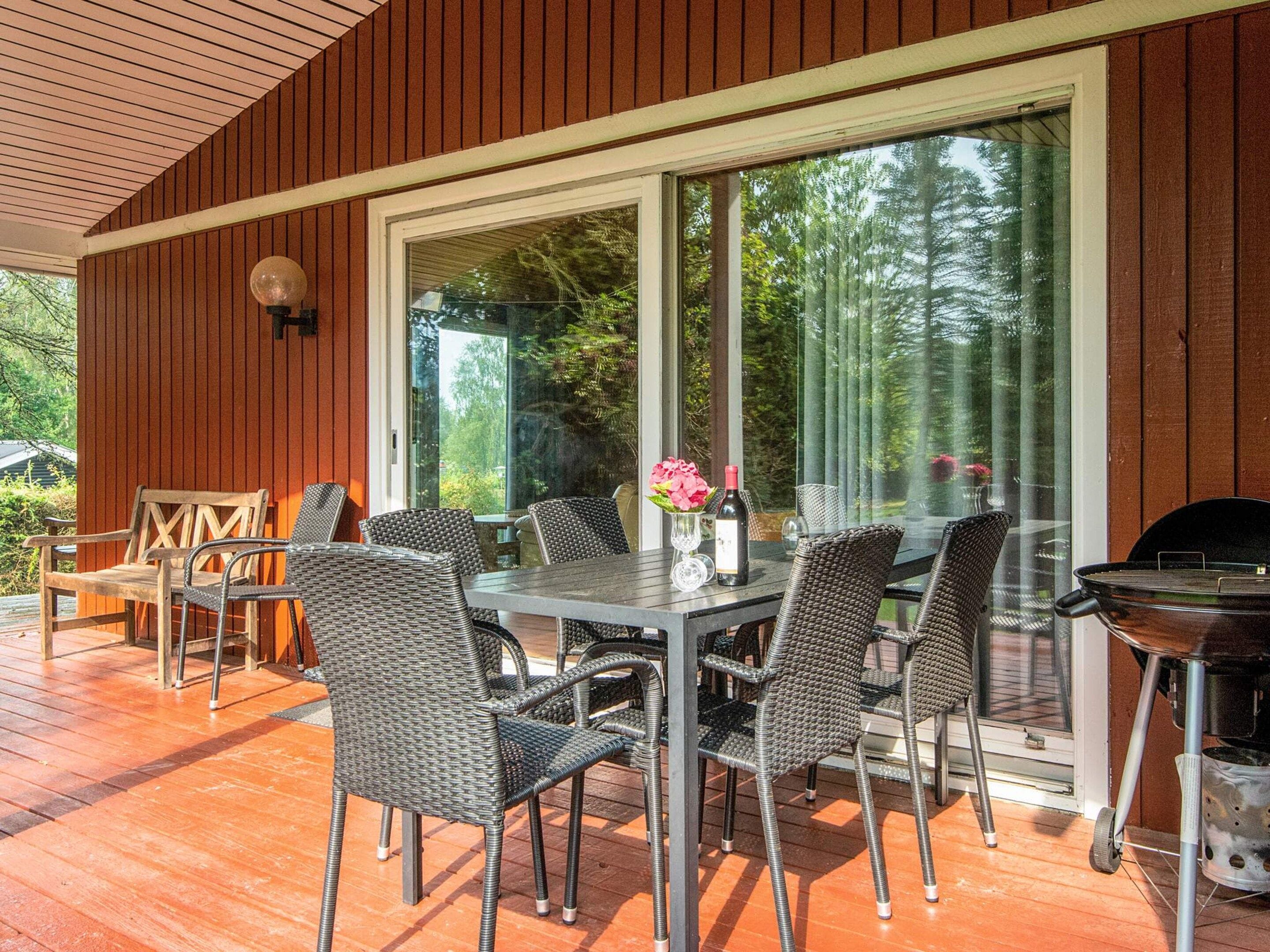 Una terrazza esterna con tavolo e sedie, un barbecue e un'ampia finestra vista alberi.