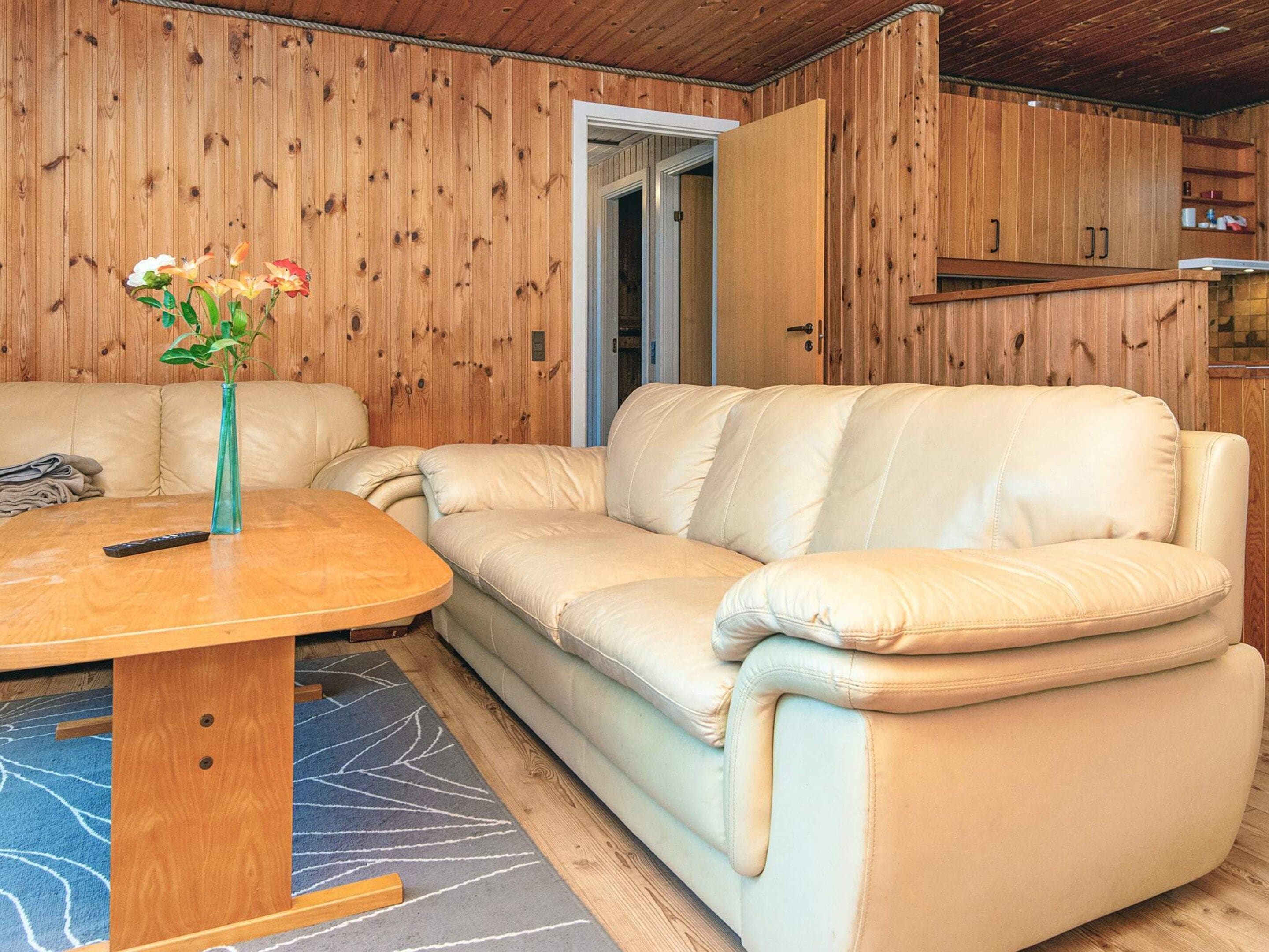 Ein Zimmer mit einem beigefarbenen Ledersofa, einem Holztisch mit Blumenvase und einer Holzwand mit einer Tür.