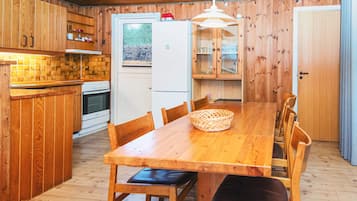 A wooden interior with a kitchen, dining table, chairs, and a refrigerator.