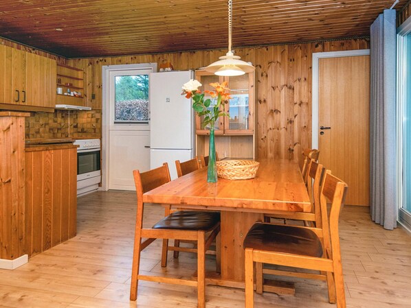 A wooden-paneled kitchen with a dining table, chairs, a hanging light fixture, and a refrigerator. - 6 Person Holiday Home in Farvang (Farvang)
