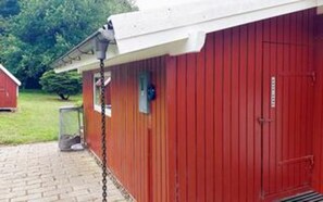 A red building with a white roof, a chain-link fence, and a metal door. - 6 Person Holiday Home in Farvang (Farvang)