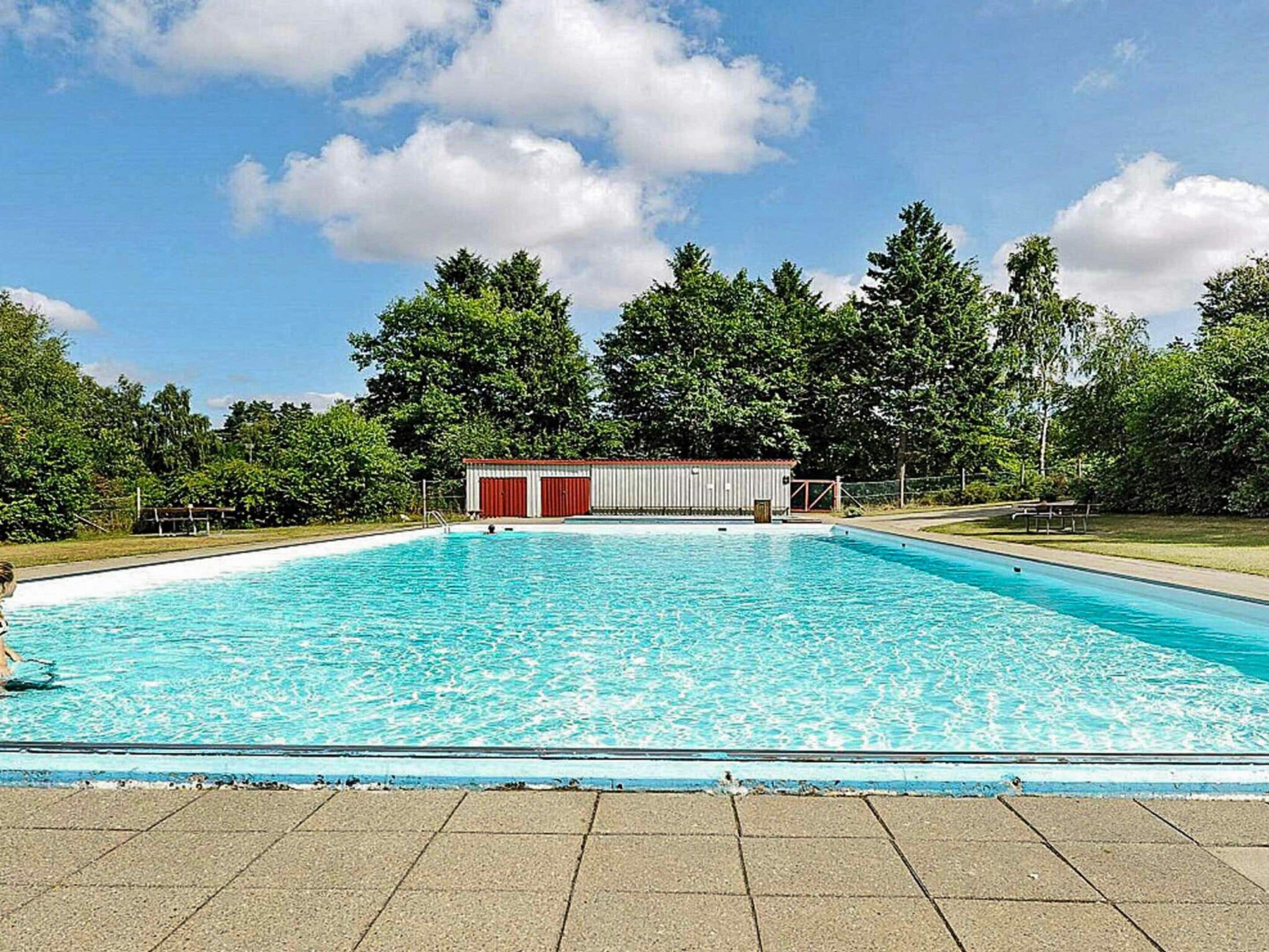 Ein rechteckiger Swimmingpool mit einer gefliesten Poolterrasse im Vordergrund.