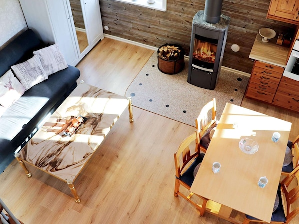 A cozy living room with a sofa, a marble coffee table, a wooden dining table with chairs, a fireplace, and a kitchen area with wooden cabinets. - 6 Person Holiday Home in Vittsjo (Vittsjo)