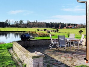 An outdoor patio with a grill, chairs, and a view of a lake and forest. - 6 Person Holiday Home in Vittsjo (Vittsjo)