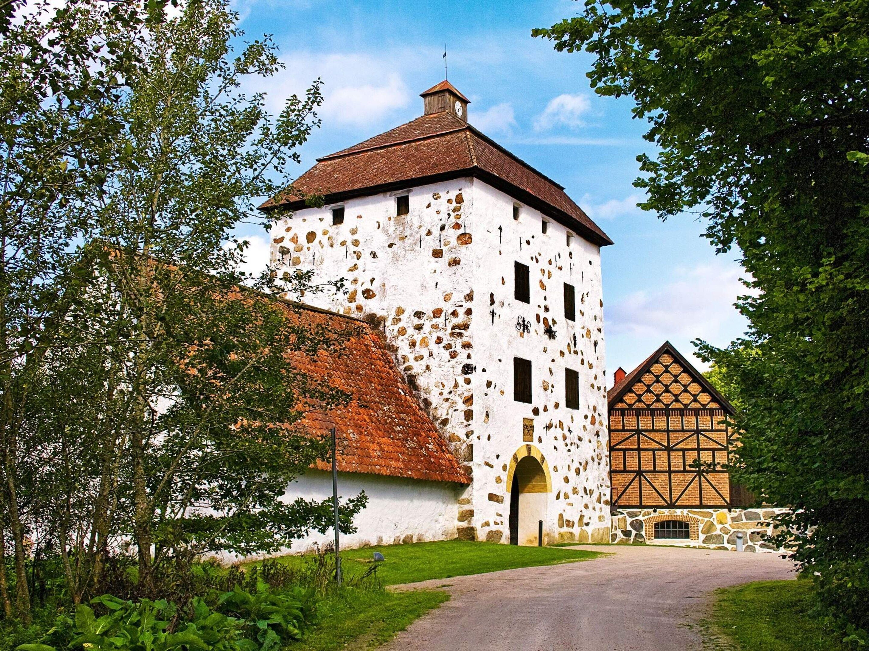 A historic building with a white facade and red-tiled roof, a stone tower, and a traditional timber-framed structure.