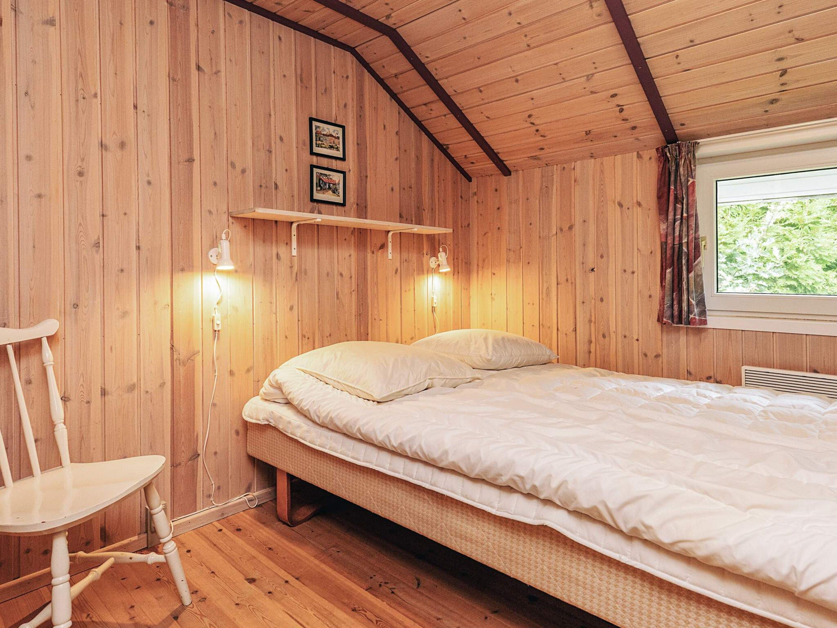 Une pièce en bois avec un lit, une chaise et une fenêtre avec des rideaux.