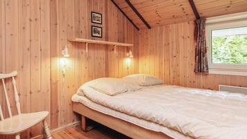 A wooden room with a bed, a chair, and a window with curtains.
