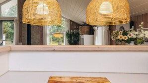 A kitchen with two woven pendant lights, a wooden cutting board, and a view of the outdoors through a window. - Holiday Home in Jerup (Jerup)