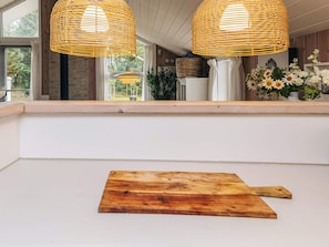 A kitchen with two wicker pendant lights, a wooden cutting board, and a window overlooking greenery. - Holiday Home in Jerup (Jerup)