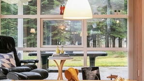Un salon moderne avec un canapé en cuir, une table basse en bois et une vue sur une forêt, visible à travers de grandes fenêtres.