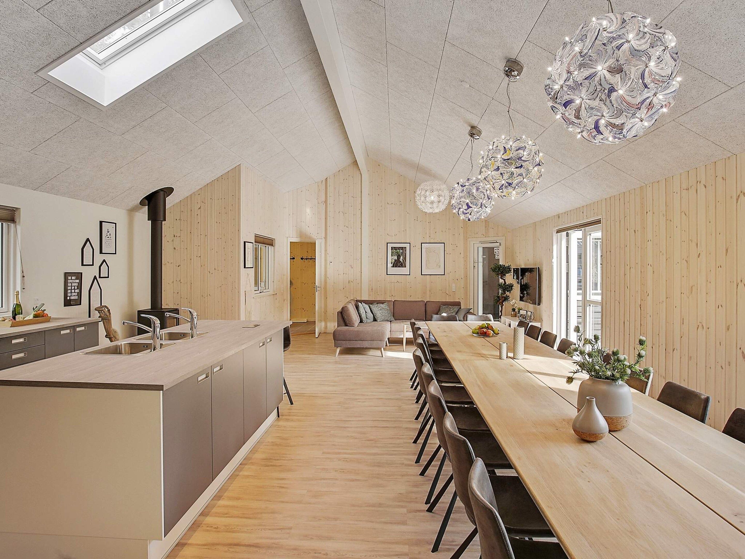 Una cocina moderna con una isla central, suelo de madera y un área de comedor con una mesa larga y sillas.