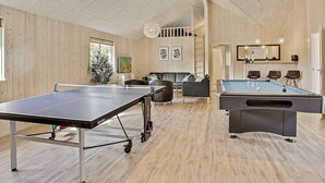 Een ruime kamer met een tafeltennistafel, een pooltafel en een zithoek met banken en stoelen.