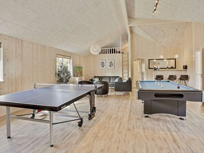 A spacious room with a ping pong table, a pool table, and a seating area with sofas and chairs.