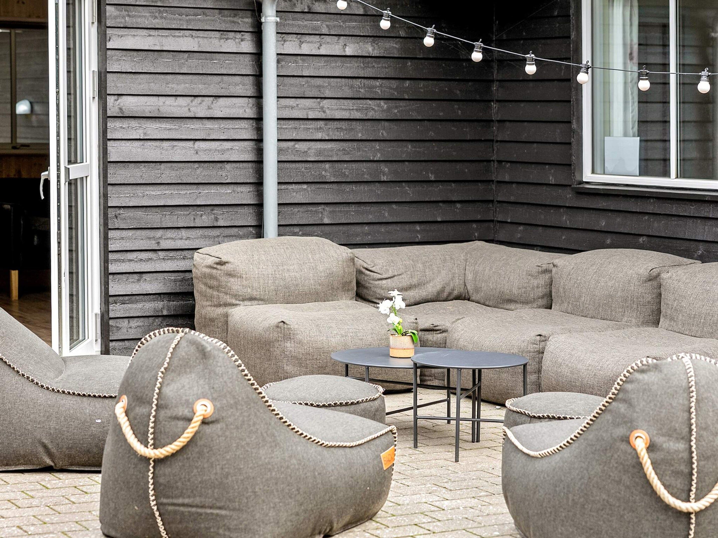 An outdoor seating area with a sofa and chairs, a small table with a vase, and string lights.