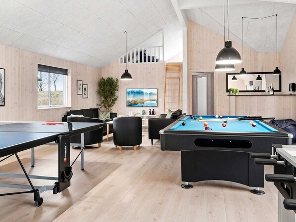 A pool table, a ping pong table, and a billiards table in a room with wooden walls and a high ceiling.
