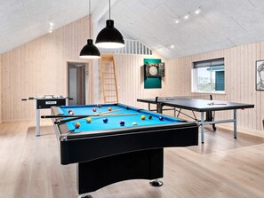 Ein Raum mit Billardtisch, Kicker, Dartscheibe und einer Dartscheibe mit Uhr.
