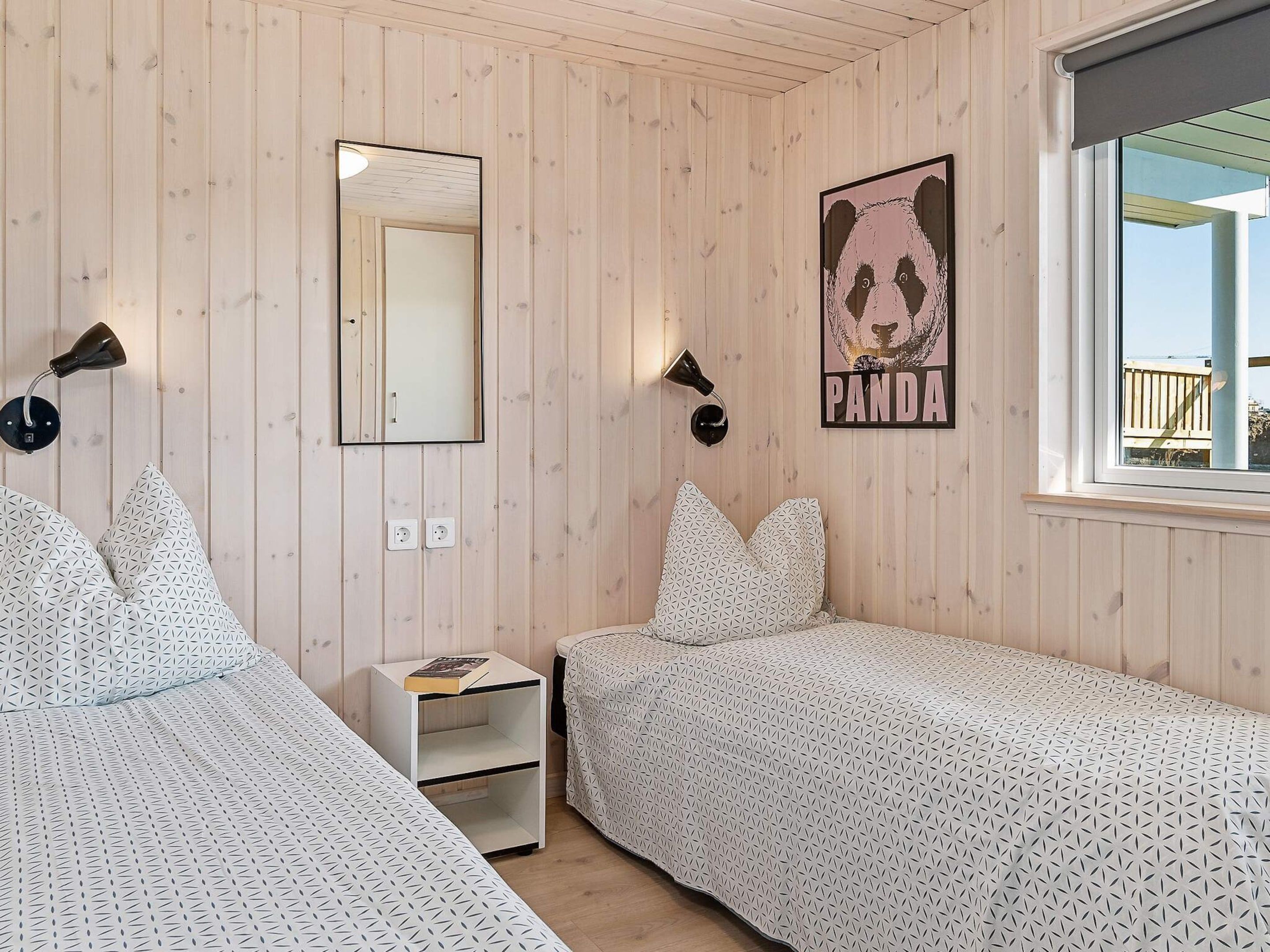 A room with two beds, a mirror, a panda poster, and a window.